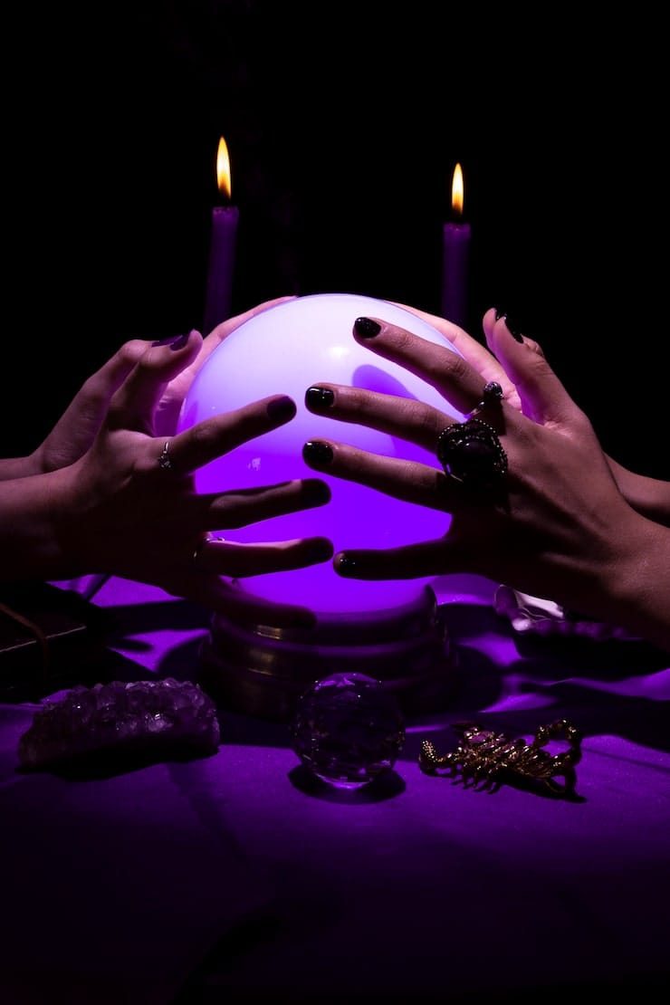 Mains posées sur une boule de cristal éclairée de violet, entre deux bougies